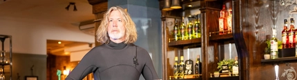 An image of a person sat on a surfboard on top of an interior bar advertising Greene King events to raise charity money for Grassroots.