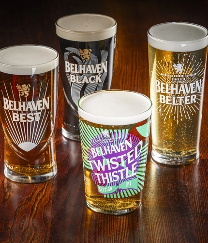 A close up view of Belhaven Belter, Belhaven Best, Belhaven Black, and Belhaven Twisted Thistle, each served in their own branded glass and standing on a wooden table.