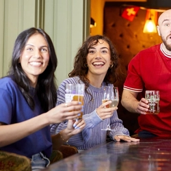 A mixed group of people, sitting at an indoor table reacting to sport event.