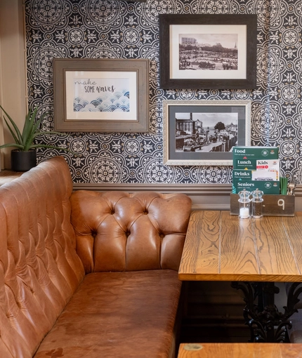 An interior restaurant seating area at The Woolpack Inn; with an upholstered booth seat, and framed artwork on the wall.