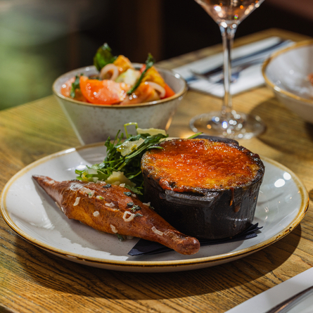 An advertising image showing a plated Lasagna main dish sat on a table within the interior restaurant seating area at The Four Oaks.