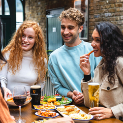 People standing around food eating and drinking