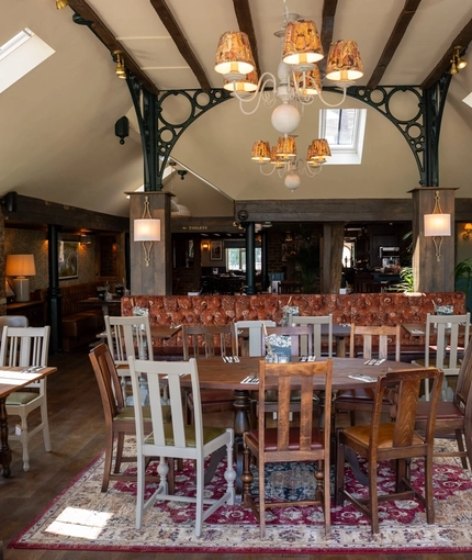 An interior restaurant seating area at The Green Man in Great Offley, with wooden flooring, upholstered booth seats, and windows in the high ceiling.