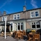 The exterior facade, signage, and seating area at The Horsforth in Horsforth, with wooden picnic tables, shade umbrellas, and string lights over the seating area.