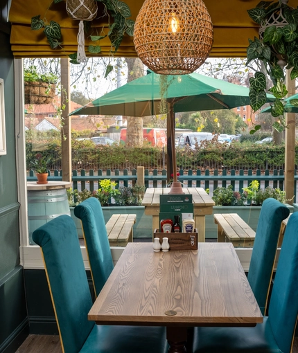 A close up view of one of the restaurant tables beside a large window inside The Grosvenor, with potted plants hanging above the table, and a view of the tables and shade umbrellas outside.