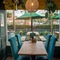 A close up view of one of the restaurant tables beside a large window inside The Grosvenor, with potted plants hanging above the table, and a view of the tables and shade umbrellas outside.