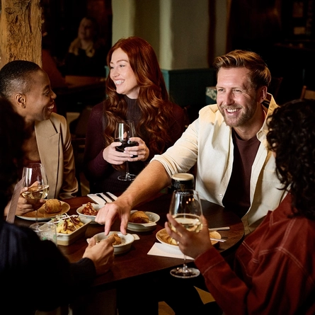 A lifestyle image showing a group of friends sat at a table within the interior seating area enjoying a selection of drinks and picky bits at a Chef & Brewer venue.