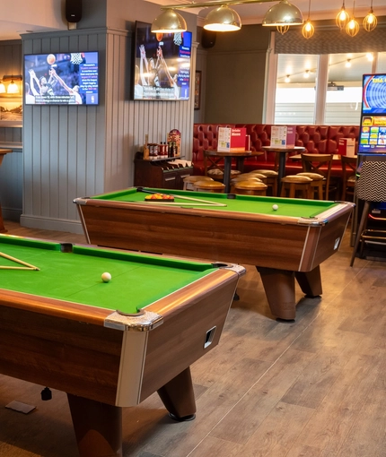 The interior games area at the Devonshire Arms, with two pool tables, TVs on the walls, and restaurant seating.