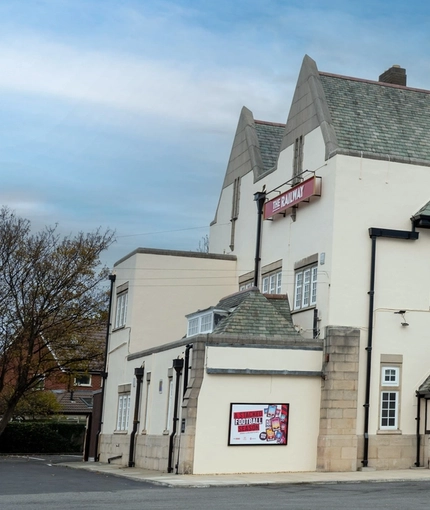 A view from across the street of the exterior facade, signage, beer garden seating area, and car park of The Railway.
