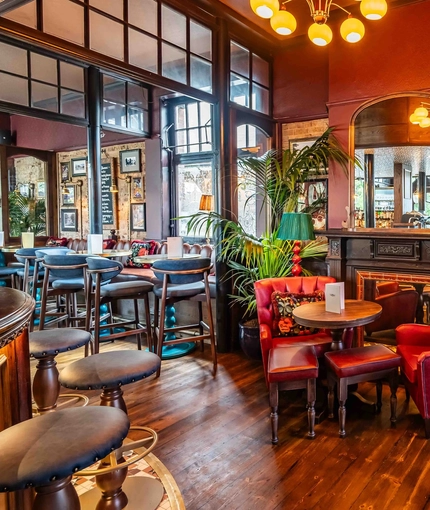 The interior seating area showing a table with 2 large chairs and stool situated next to a fireplace with large wall mounted mirror at The Duke Of Sussex.
