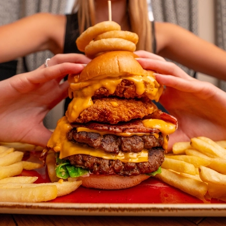 A close up image of a burger with a person in the background within the interior restaurant and seating area at a Hungry Horse venue.