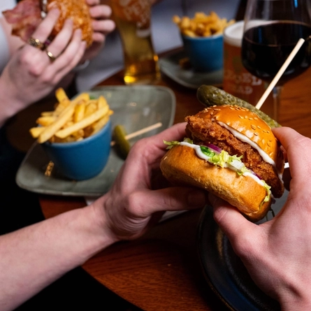 A focused image on a main burger meal served in the restaurant and seating area in a Urban Social venue with another burger meal blurred in the background and drinks served with the meals.