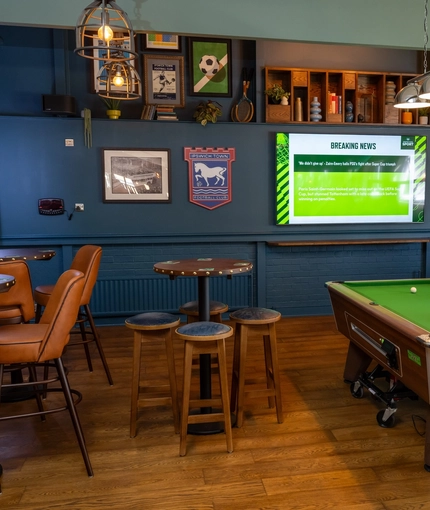 The interior seating area at The Man On The Moon, with a TV on the wall, a dartboard, and a pool table.