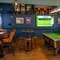 The interior seating area at The Man On The Moon, with a TV on the wall, a dartboard, and a pool table.