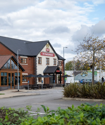 The exterior facade, signage, seating area, car park, and children's play area of The Parsonage in Leigh.