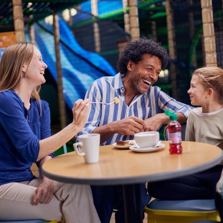 A family enjoying cake and hot drinks at a table in a Wacky Warehouse.