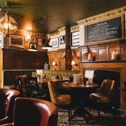 The wood panelled interior restaurant seating area at the Masons Arms in Mayfair, with a fireplace, an upholstered booth corner seat, and flowers carved into the coving.