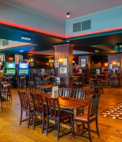 The interior restaurant seating area and bar at the Scholars Arms in Southampton; with illuminated dartboards, TVs on the walls, and gaming machines.