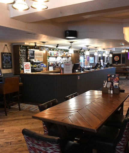 Interior dining area of a pub with a bar, two TVs, two gambling machines and a dartboard.