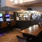 Interior dining area of a pub with a bar, two TVs, two gambling machines and a dartboard.