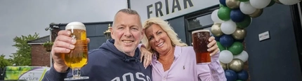 A man and woman holding pints of beer outside of a pub.