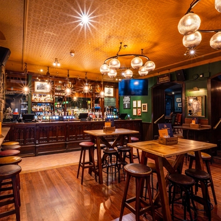 The bar and interior restaurant seating area at The Beehive Inn, with a TV hanging from the ceiling, bar stool seats, and gothic window style carving on the front of the bar.