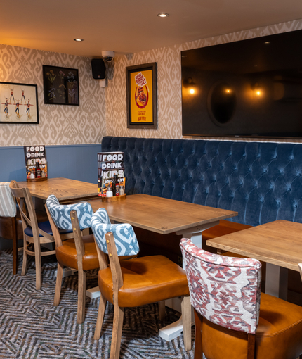 An interior restaurant seating area at The Wrekin Giant, with three tables in front of a long, upholstered booth seat, and a TV on the wall above it.