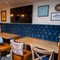 An interior restaurant seating area at The Wrekin Giant, with three tables in front of a long, upholstered booth seat, and a TV on the wall above it.