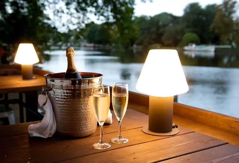 Metro - Boaters (Kingston upon Thames) - The beer garden at dusk - the table has a lamp and a bottle of champagne