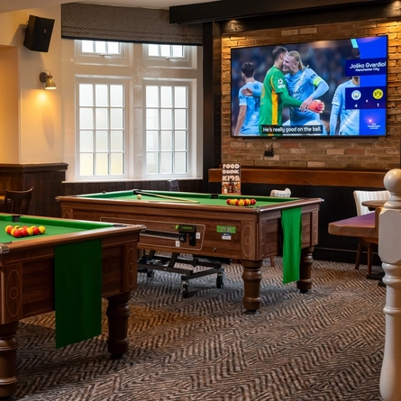 The interior pub gaming area of The Railway, with two pool tables, a TV on the wall, and restaurant tables.