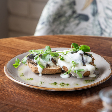 A Non-Gluten Containing Ingredients creamy garlic mushrooms starter, served on a plate which sits on a wooden table.