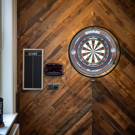 A close up view of the illuminated dartboard on the wall inside The Victoria, with a score board on the wall beside it.