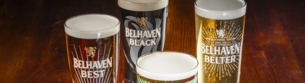 A close up view of Belhaven Belter, Belhaven Best, Belhaven Black, and Belhaven Twisted Thistle, each served in their own branded glass and standing on a wooden table.