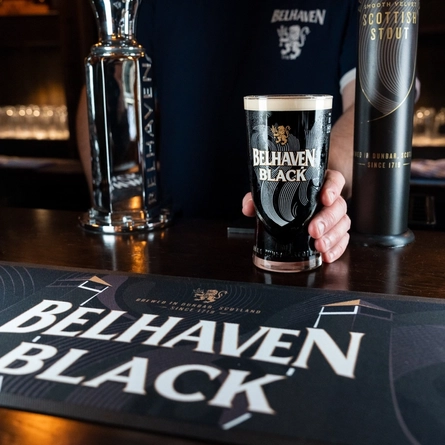 A lifestyle image showing a member of staff placing a pint of Belhaven Black onto a wooden bar top.