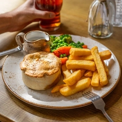 A lifestyle image showing a person sat at a table enjoying a pint of Greene King IPA and a Mushroom & Ale Pie dish within the interior restaurant seating area at a Chef & Brewer venue.