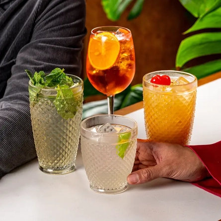 Four cocktails on a table, with a hand holding one of them.