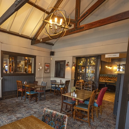 The interior restaurant seating area at the Paper Mill in Pilsworth; with a fireplace, wooden beams on the vaulted ceiling, and a TV on the wall.