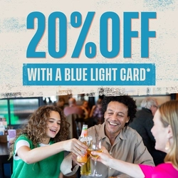 Promotional graphic for Flaming Grill venues showing the text ‘20% OFF with a Blue Light Card’ above a scene of three people sitting at a restaurant table, raising drinks in a toast. Plates of food, including a steak and vegetables, are visible on the table, with a busy restaurant environment in the background.