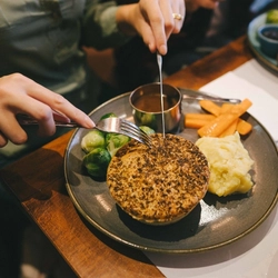 A pair of hands holding cutlery over a plated meal on a festive decorated table.