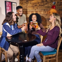 An image showing 4 friends at a table enjoying drinks and celebrating with a cheers within the interior seating area at a Flaming Grill venue.