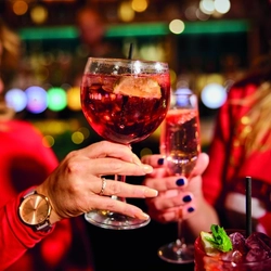 An image of 2 people holding cocktail style drinks celebrating with a festive cheers within the interior of a Greene King Pub venue.
