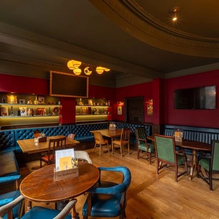 An interior restaurant seating area at The Beehive Inn, with upholstered chairs and booth seats, ornaments on illuminated shelves, and TVs on the walls.