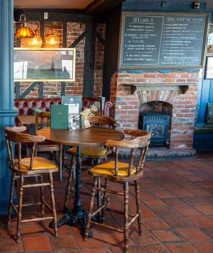An image of the interior restaurant seating area with tables, chairs, brick log burner fireplace and tiled flooring at The Spice Island.