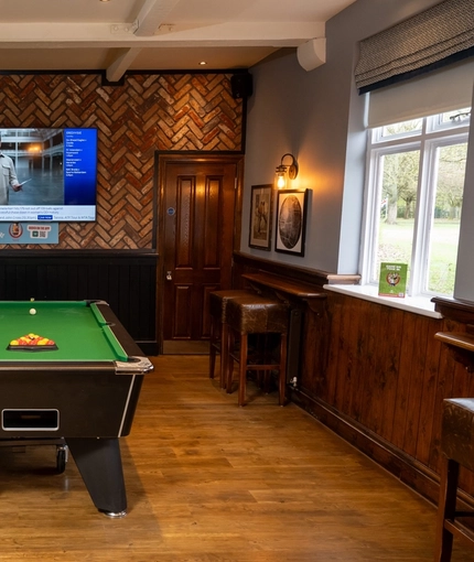 The interior games area at The Hussey Arms in Brownhills, with a pool table, a TV on the wall, and bar stool seating.