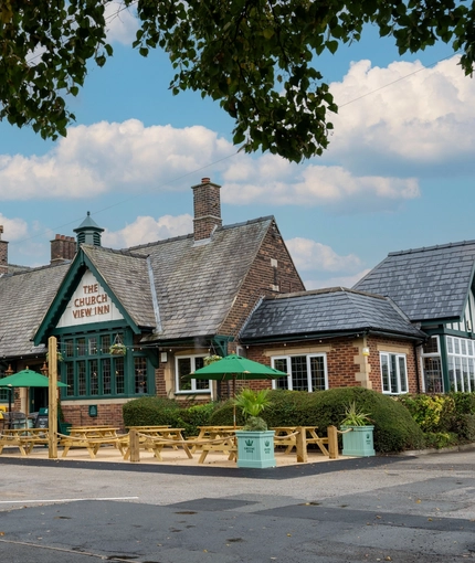 The exterior facade of the venue, car park, venue signage and wooden bench outdoor seating area at The Church View Inn.