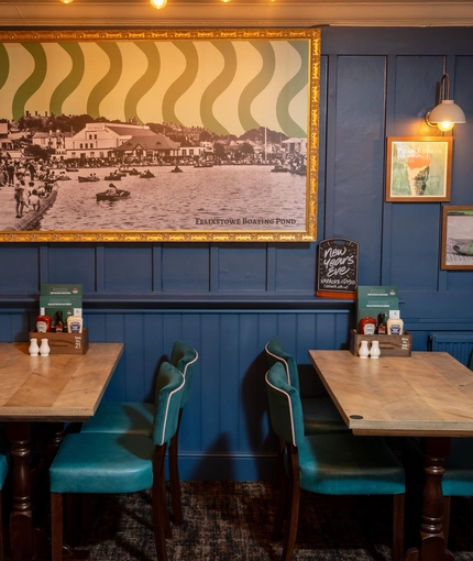 An interior restaurant seating area at The Grosvenor, with framed artwork on the wall, and upholstered chairs.