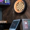 The darts area inside the Clocktower in Milton Keynes, with a dartboard, a TV on the wall, and a close up view of the electronic scoring system sitting on a table.