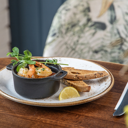 A Non-Gluten Containing Ingredients king prawns starter, featuring king prawns in a small dish served on a plate with slices of bread and a lemon wedge.
