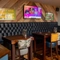 An interior seating area at The Kittoch in East Kilbride, with a long, upholstered booth seat, a TV on the wall above it, and wooden tables with upholstered bar stools.