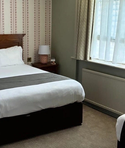 An image showing the interior of one of the hotel rooms featuring a double bed, bedside cabinets either side with lamps and single bed at The Antelope.